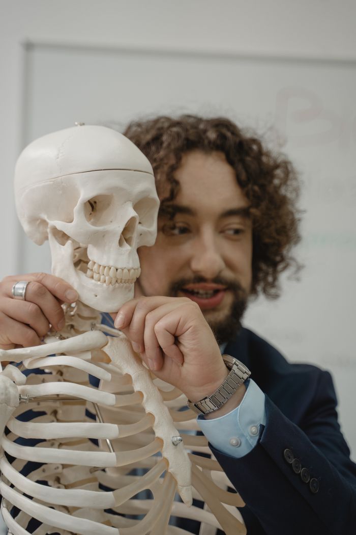 Teacher discussing human skeleton anatomy in a classroom setting, highlighting bones and skull.