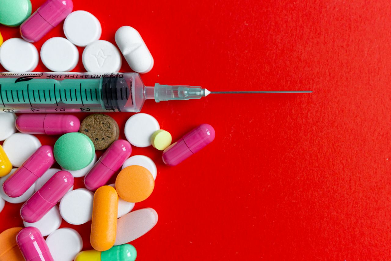 Top view of various colorful pills and a syringe on a vivid red surface, highlighting medical themes.